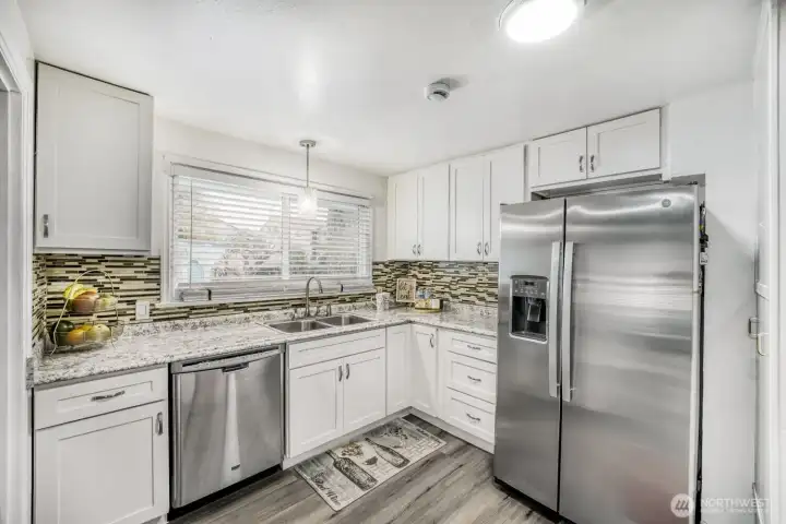 Updated kitchen with white cabinetry, granite countertops, stainless steel appliances, and designer backsplash.