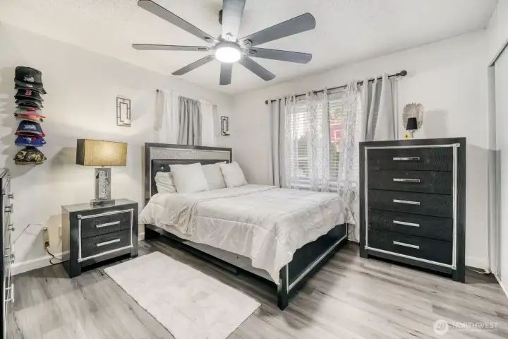 Spacious primary bedroom with modern flooring, ceiling fan, and soft natural light.