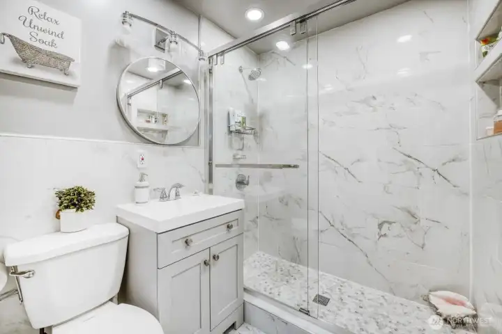 Fully renovated bathroom with glass walk-in shower, marble-style tile, and modern vanity.
