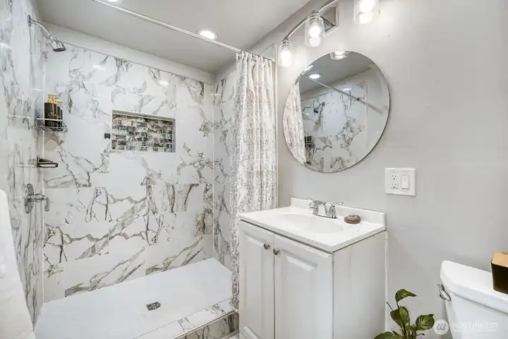 Beautiful tiled, walk-in shower with decorative niche and elegant marble-style surround.