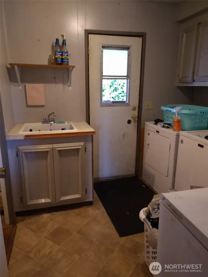 Current photo of laundry room with sink and back door.