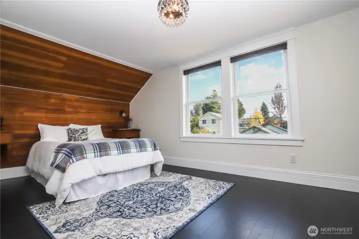 Cozy but roomy primary bedroom with paneling, built-in nightstands and lighting.