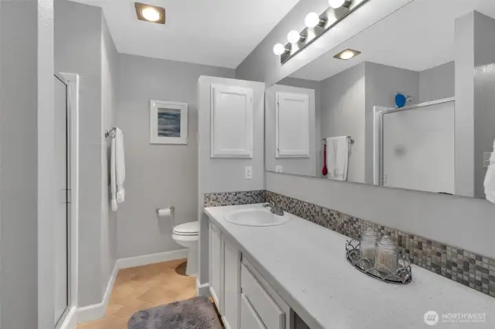 Well-lit primary three-quarter bath has a large vanity with loads of personal storage space and walk-in shower stall.