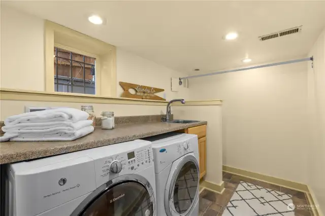 Laundry room on the lower level has a folding area, sink, drying rack and toilet.