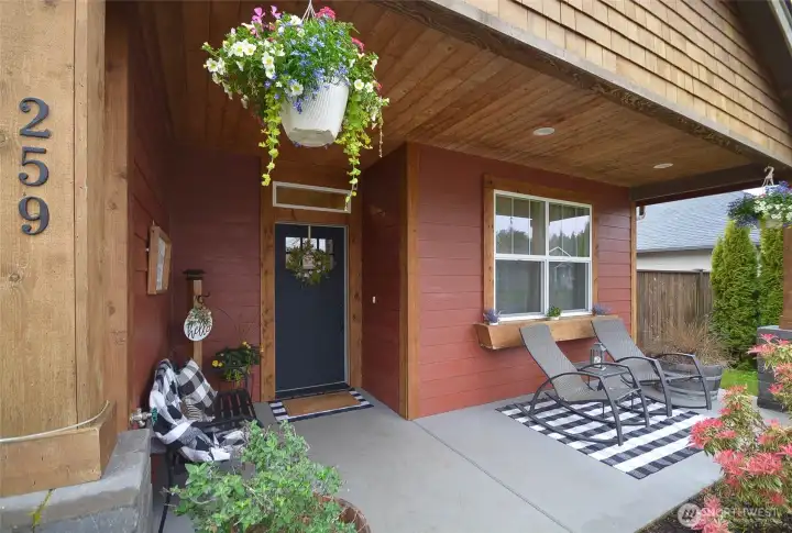 “Covered front porch featuring pine inlay ceiling with integrated can lighting, supported by stone pillars on a solid poured concrete base.”
