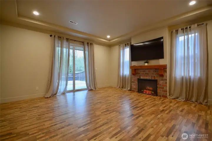 Spacious living room featuring an electric fireplace with a wood mantel and stone inlay, abundant natural light from large windows, and a sliding glass door leading to the covered back patio.
