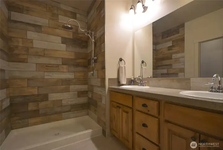 Primary bathroom featuring a double-sink vanity with custom alder wood cabinetry, offering abundant drawer and cabinet storage. Includes a walk-in shower with tile inlay surround and tile flooring.