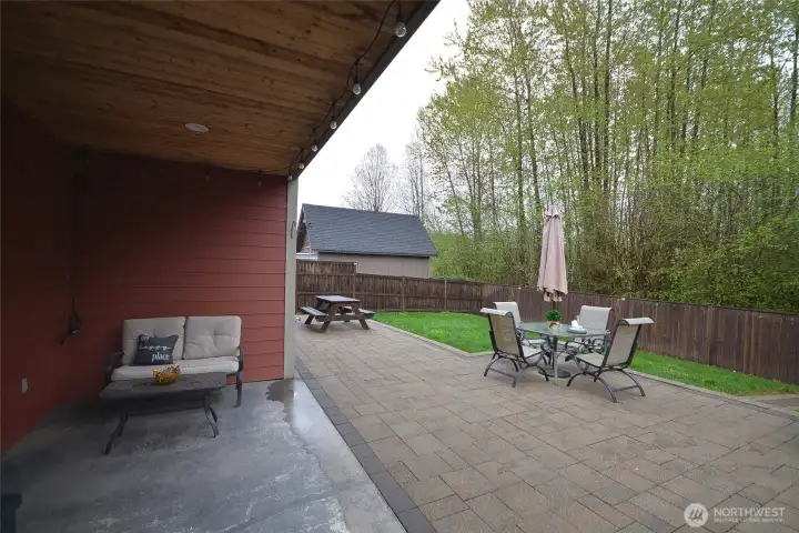 Covered back concrete patio featuring pine inlay ceiling with can lighting—perfect for outdoor entertaining and BBQs. Includes an extended paver patio with a stone fire pit, steps leading to the grassy area, and a gate providing direct access to nearby trails and park.