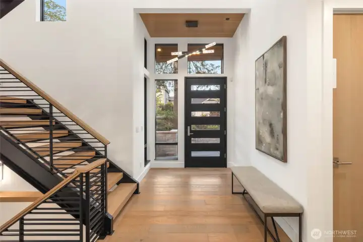 Statement and light drenched entry features custom glass panneled stained door, designer selected hanging light fixture and wood ceiling detail, and floating steel stairs with hardwood treads