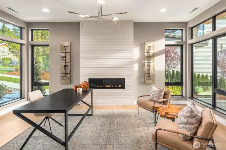 Statement main floor study off the entry features a designer selected full height custom tile fireplace surround, floor to ceiling windows with lake views, and custom built in cabinets and shelving with luxury slab countertops