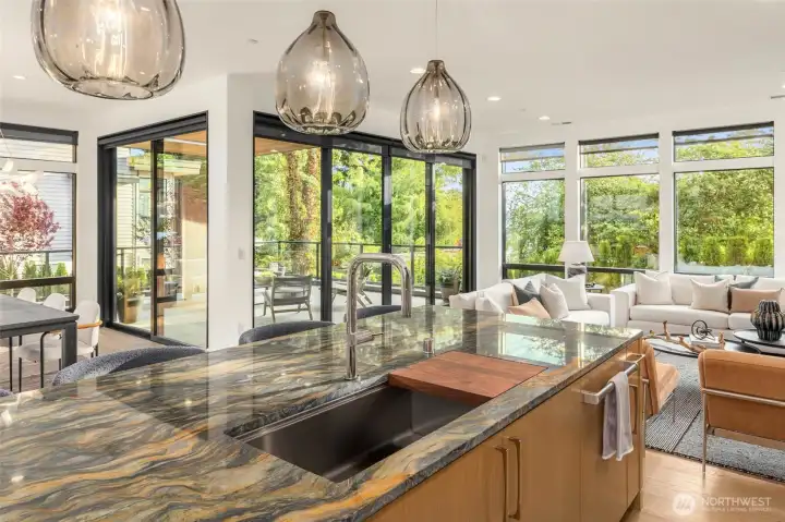 Oversized center island accentuated by designer smoked glass pendants and custom steel sink with built in walnut prep board