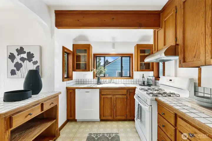 Kitchen with tile countertops, new dishwasher and range hood and lots of cabinet/storage space.
