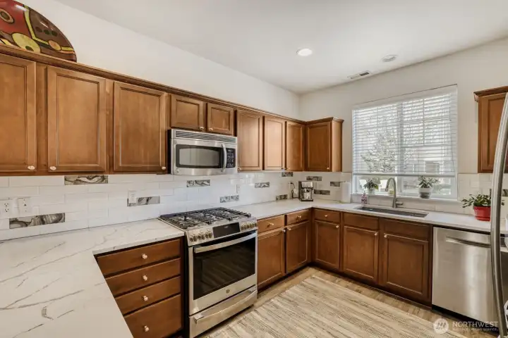 A kitchen that any chef would dream of with abundant cabinets, stainless steel appliances and gorgeous quartz countertops with decorative tile backsplash.
