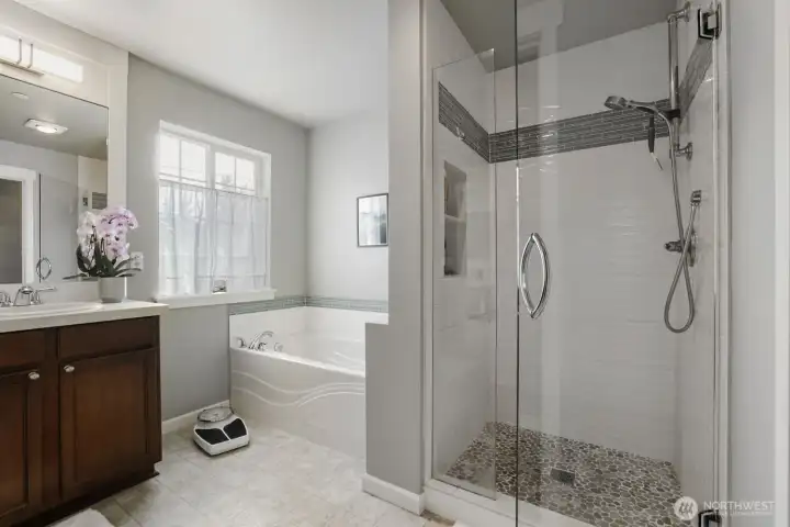 The remodeled walk-in shower has new frameless glass doors, stone tile floor and decorative tile surround with new fixtures.