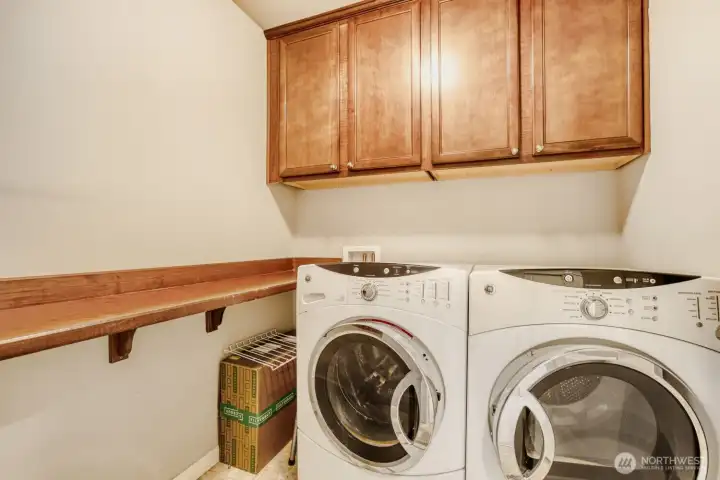 Convenient upper floor utility room with a full-size washer and dryer, shelving and cabinets.