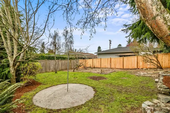 Side view of back yard including this handy concrete based clothes line and established flower beds