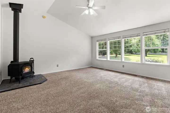 Inviting living room with vaulted ceilings, cozy wood stove, and a wall of windows that fills the space with natural light.