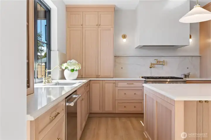 Floor-to-ceiling white oak hutch, brass pot filler, quartz backsplash behind the Thermador range.
