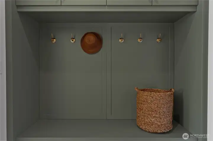 Built-in mudroom with brass hooks, sage green cabinetry, and bench seating.