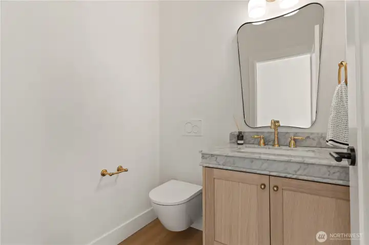 Powder room with Venetian plaster walls, Carrara marble vanity top, wall-mount toilet, and white oak cabinetry.