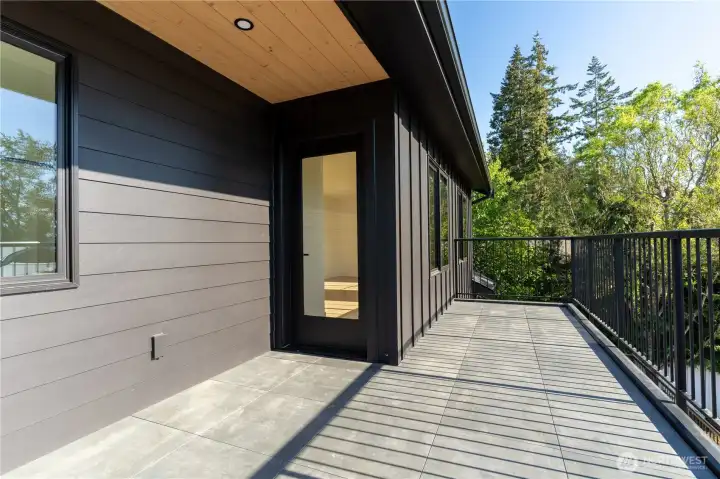 Private balcony off the primary bedroom with porcelain pavers, iron railing, and nickel gap fineline soffit.