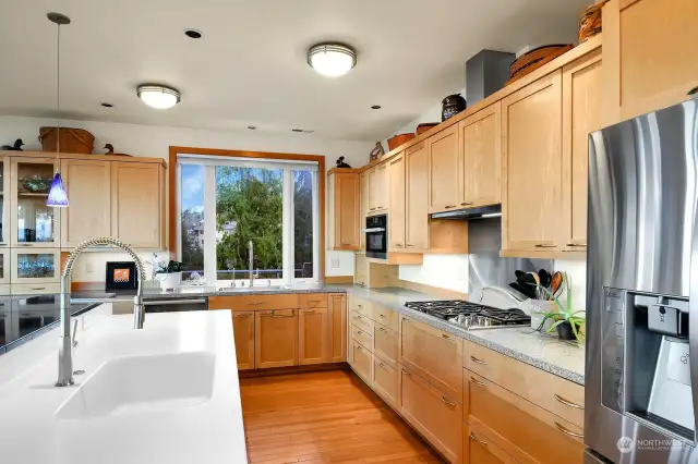 This kitchen has ample storage, an island with a built-in sink, a separate main sink, a premium Wolf gas cooktop, a Miele speed oven, dishwasher, and a sleek Miele cooktop vent.