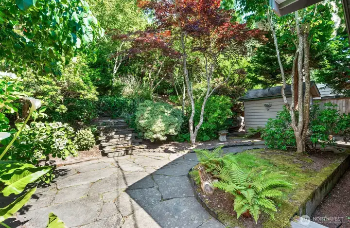 This backyard is a beautiful oasis with a stone patio and a stairway leading through the back terraced part of the yard.