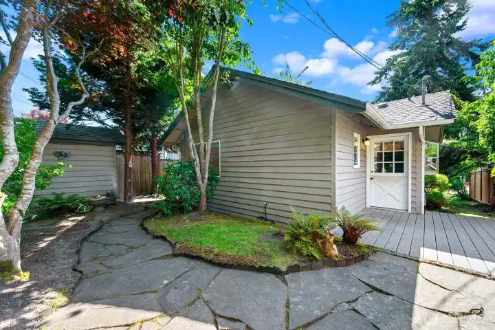 The stone patio leads to a storage shed on the side of the yard.