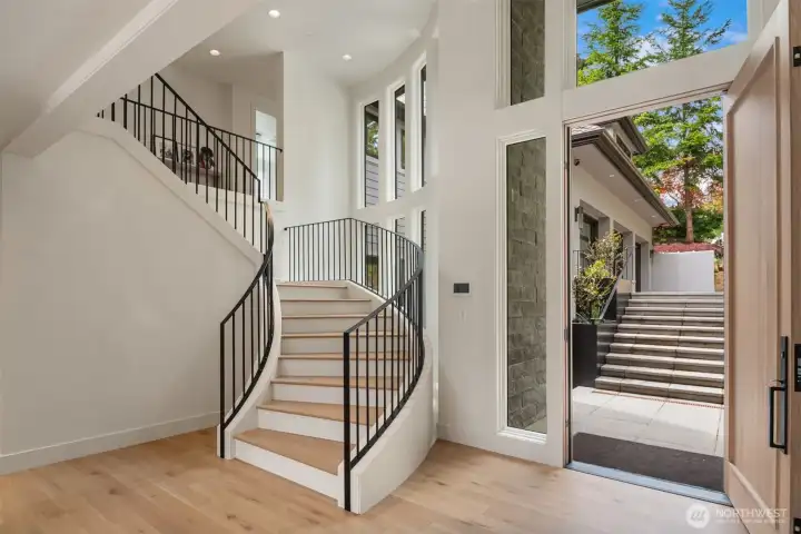 Grand entryway with soaring ceilings, sweeping staircase, and walls of windows that fill the space with natural light.