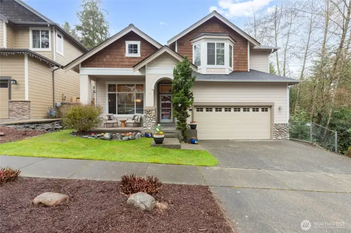 Pacific Northwest craftsman, showcasing a sophisticated blend of cedar shingle siding, stacked stone accents, and a charming bay window. The manicured lawn and covered entry create a warm and inviting first impression.