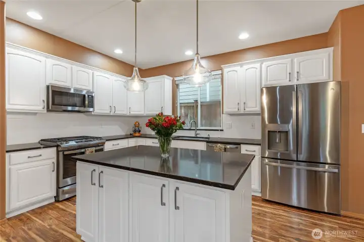 Stainless steel appliances, including a high-performance gas range and French door refrigerator, complement the elegant brushed-bronze hardware and designer pendant lighting.