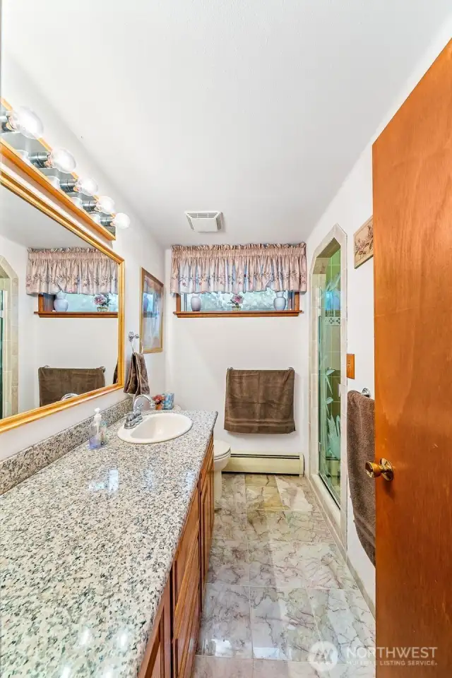 Lower-level bathroom with granite counters, marble flooring and a walk in tiled shower.