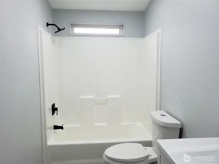 A View of the Main Guest Bath Room Showing New Vanity, Sink and Faucet, a Lighted Mirror, New Toilet, Tub Shower. Paint, Trim and Vinyl Plank Flooring.