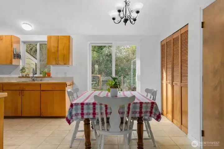 Bright kitchen and dining area with ceramic tile flooring, wood cabinetry, and sliding glass doors opening to a private deck and backyard.
