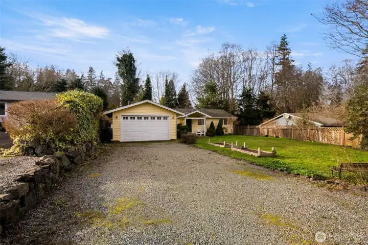Long gravel driveway leading to a detached two-car garage with additional space for storage or workshop use.