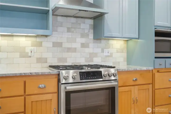 Stainless steel gas range framed by custom cabinetry, elegant tile backsplash, and under-cabinet lighting for a bright, inviting workspace.