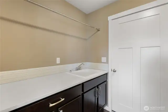 Laundry Room with quartz countertop & glass mosaic backsplash, sink & space for hanging clothes