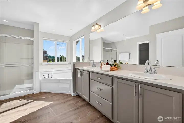 Bright ensuite featuring a large soaker tub, double vanity, walk-in shower, and abundant natural light from double windows.