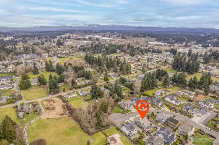 Panned out aerial shot of home showing nearby greenery and homes.