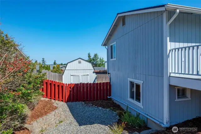 Sloped side yard on the N side of house with a gate to access the shed in back.