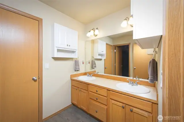 Primary bathroom with dual sinks, shower/tub combo, and laminate flooring.  Door leads to a small room with a window that could be used for maybe a reading room, an office, a second walk-in closet or a storage room.