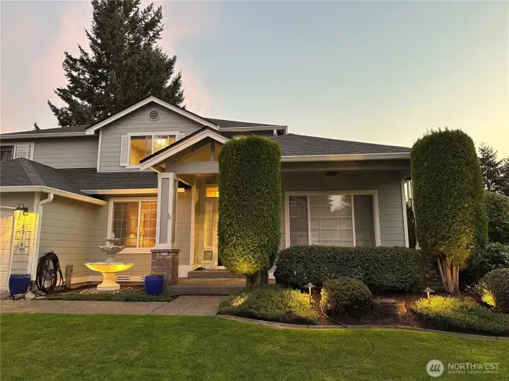 Exterior lighting highlights the water fountain, bushes and tree in the front yard