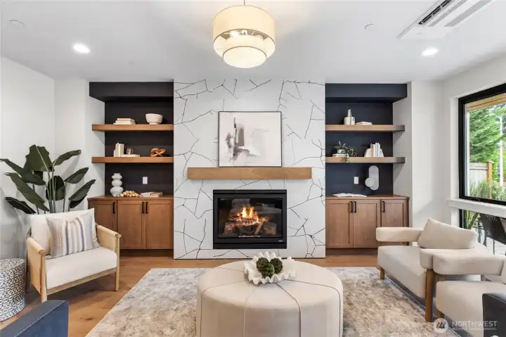 The fireplace serves as a stunning focal point, framed by a white and gray geometric surround that adds texture and visual interest to the room. Above it, add your favorite art piece or TV, anchoring the space with modern flair. Flanked by built-in shelving and cozy armchairs, the fireplace creates a natural gathering spot that balances style and warmth.