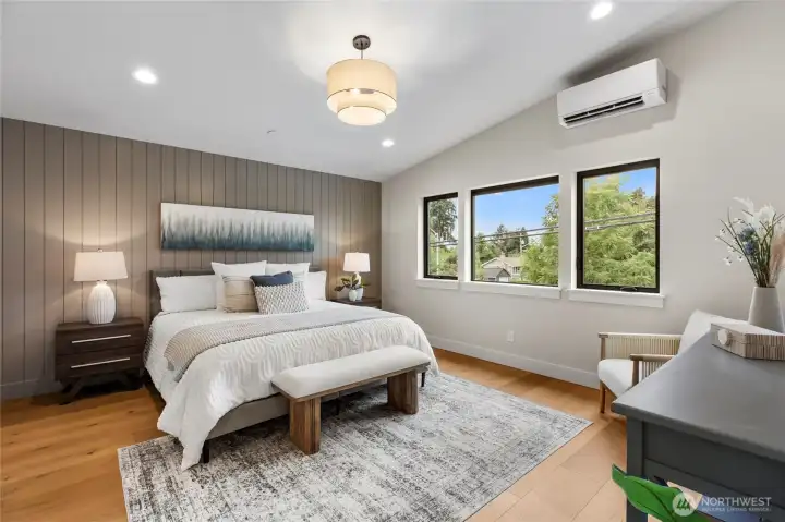 This spacious bedroom exudes calm and comfort, with soft gray walls, warm wood accents, and abundant natural light from oversized windows. The layered textures and clean lines create a serene retreat that feels both luxurious and inviting.