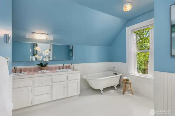 Full bathroom, adjacent to the second bedroom, features vintage tile, painted wood floors, wainscoting, and a clawfoot tub.