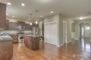 From this angle, you get a peek at the perfect flow of this home. The kitchen is framed beautifully by tall ceilings and stunning hardwood floors, while the pantry closet adds functionality without sacrificing style. The entry to the powder room offers convenience, and the arched doorway to the formal dining room adds just the right touch of elegance. Beyond that, another large arched doorway leads to the entry foyer, completing the open feel of this well-designed space.