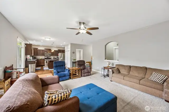This family room is all about comfort and cozy vibes. The neutral-toned carpeting cuts down on noise, perfect for movie nights when you need that surround sound without the neighbors knowing your entire plotline. High ceilings make the space feel extra roomy, and an arched cutout in the hallway adds a touch of charm as it leads you to the laundry and garage. Across the room, you have the casual dining space in front of the slider, and of course, the kitchen. It is the perfect spot to relax or entertain without missing a beat.