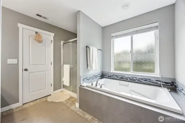 This primary suite bathroom is all about indulgence. The glass door shower is sleek and stylish, while the deep soaking tub sits underneath a large privacy glass window, offering natural light and ventilation when you need it. The wide slat blinds give you control over privacy, while the grey tile surround with a glass tile accent adds a modern touch. With a 5-piece layout, this bathroom has space, style, and all the right features for relaxing after a long day.