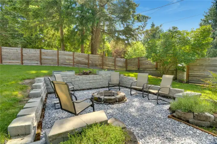 The firepit is ready for summer evenings enjoying s'mores and laughs with friends. Mature trees and fencing help create a sense of privacy throughout the yard.
