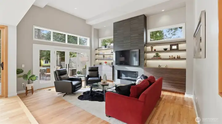 The adjoining family room is the heart of the home—anchored by a striking floor-to-ceiling gas fireplace framed by sleek floating shelves and built-ins, creating a warm, inviting gathering space. French doors open to expansive composite deck.